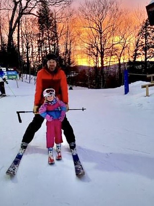 An adult and child on skis at sunset